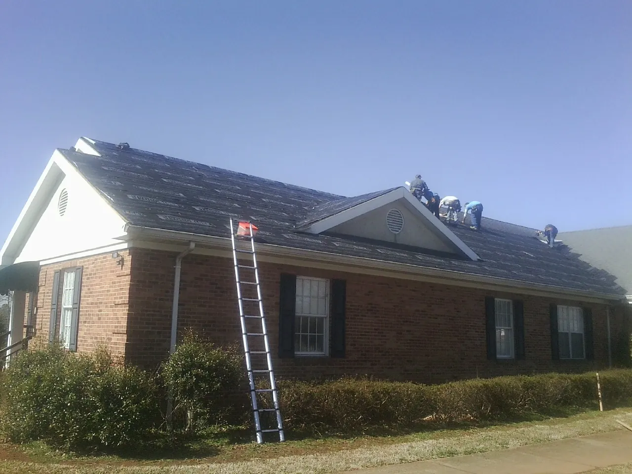 Crew tearing shingles off a brick ranch roof with a ladder set — Metal Roof Repair work by our crew in Bellevue