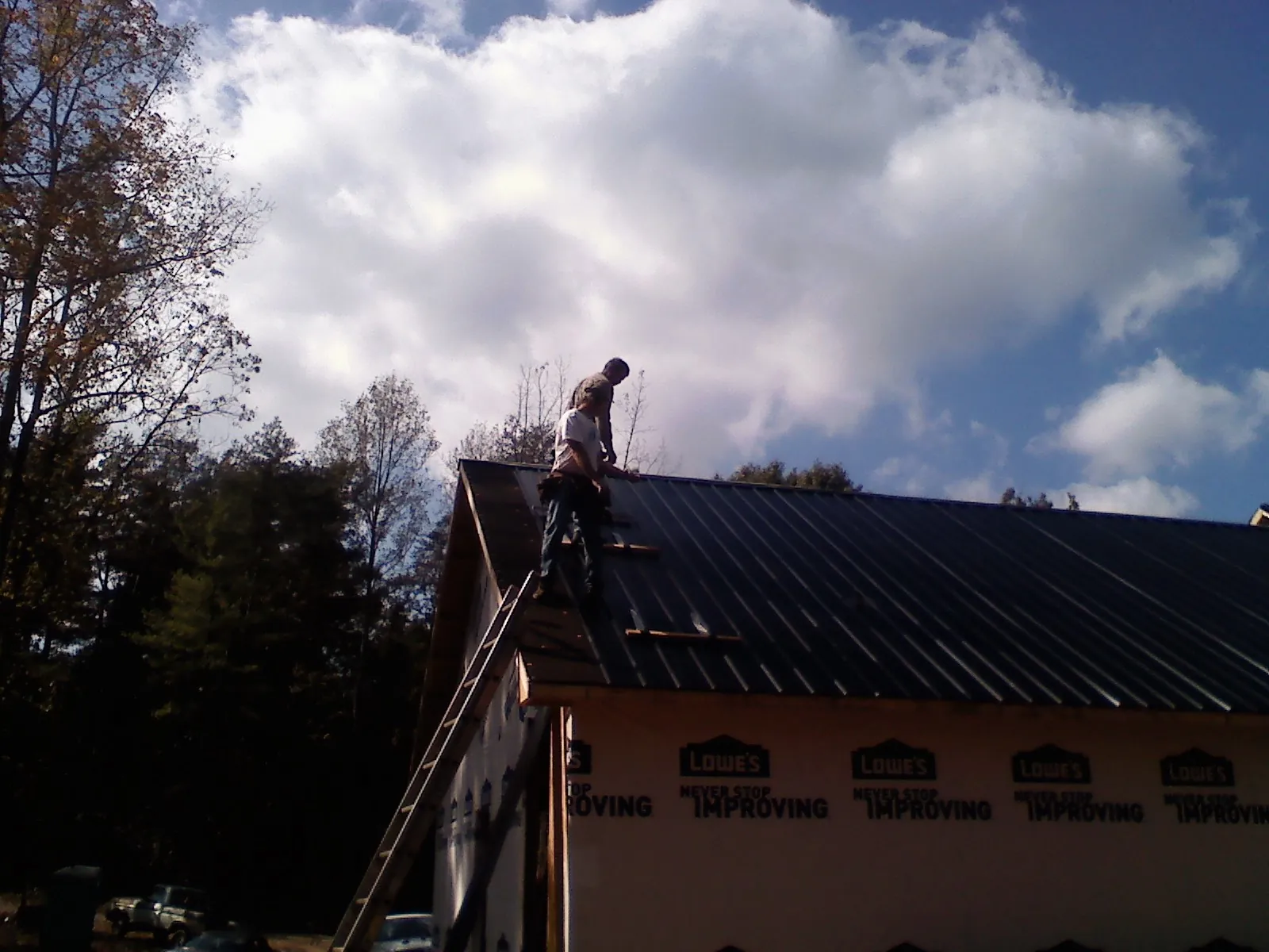 Roofer fastening dark metal panels high against a cloudy sky, from a Roof Inspection job in Bellevue
