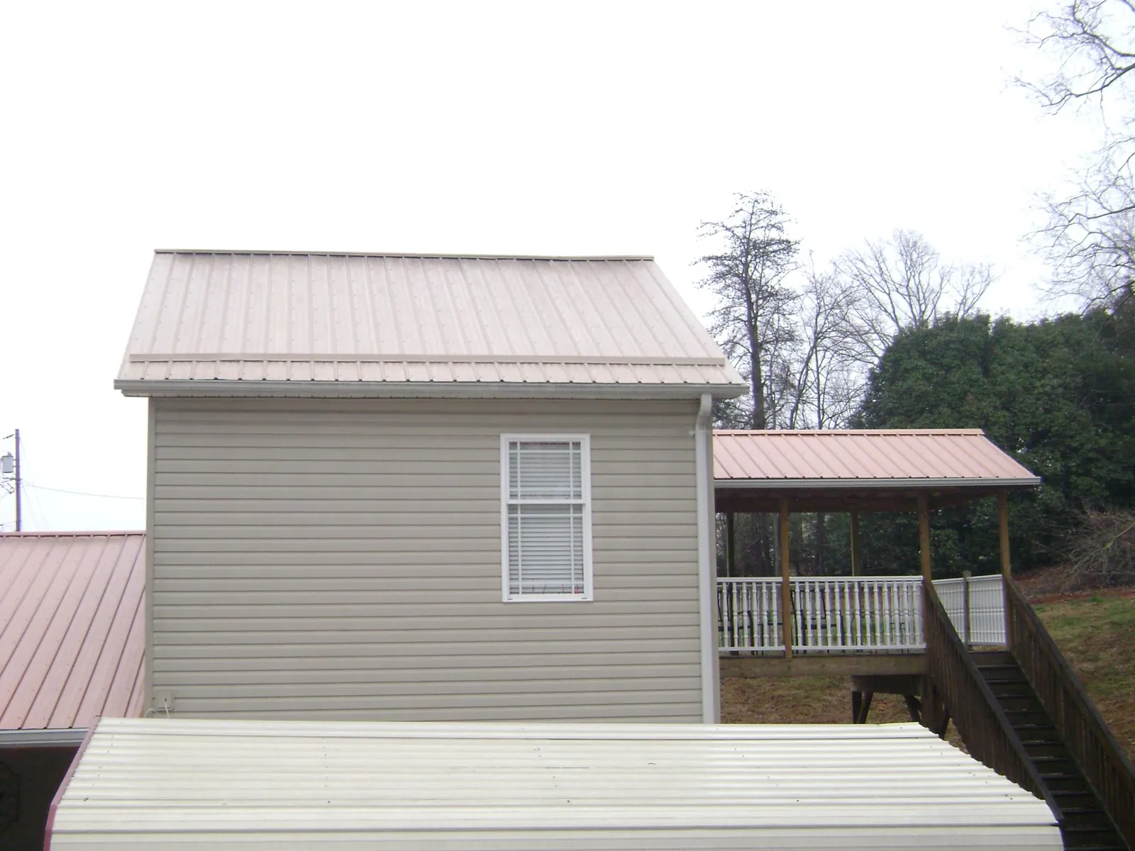 Tan metal roofs on a two story addition and attached porch, from a Roof Replacement job in Bellevue